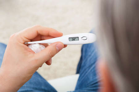 Portrait of a sick man looking at thermometer