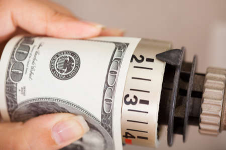 Close-up Of Female Hand Adjusting Thermostat Covered With Banknoteの写真素材