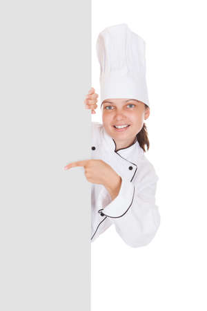 Female chef pointing on blank placard over white backgroundの写真素材