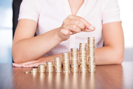 Close-up Of Businesswoman Stacking Gold Coins On Increasing Coinsの写真素材