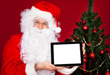 Portrait of a happy santa holding digital tablet over red backgroundの写真素材