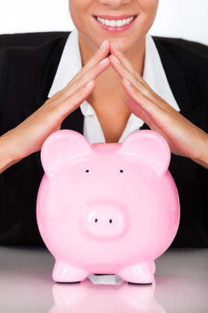 Young Happy Businesswoman Holding Pink Piggy Bank At Deskの写真素材