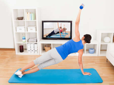 Young Woman Exercising On Mat In Front Of Televisionの写真素材