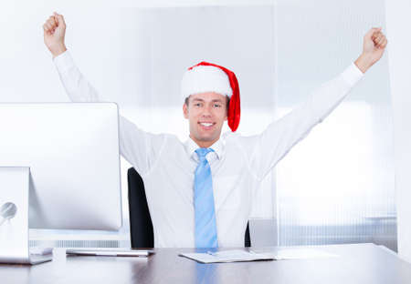 Happy Young Businessman Wearing Santa Hat Using Computer In Officeの写真素材