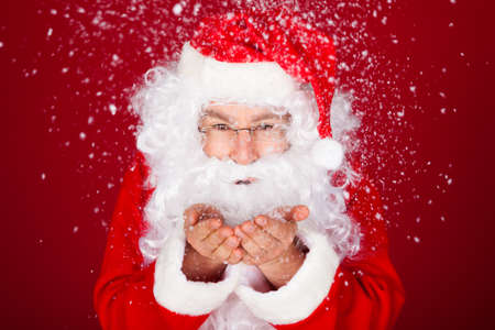 Portrait of santa blowing snow over red backgroundの写真素材
