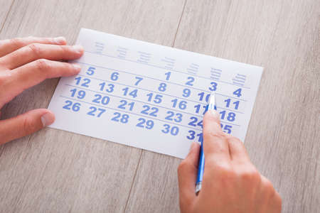Close-up Of Man Marking With Pen And Looking At Date On Calendarの写真素材
