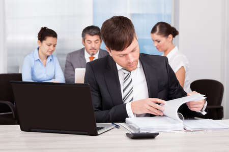 Happy Businessman Sitting In Front Of His Colleagues Working At Desk
