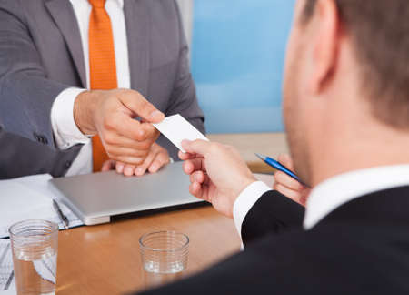 Close-up Of Two Businessmen Holding Card Over Deskの写真素材