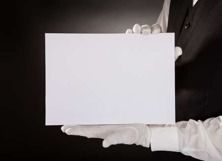 Closeup Of Young Waiter Presenting Blank Placard Over Black Background