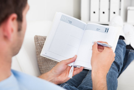 Close-up Of A Young Man Sitting On Couch Writing In Diaryのeditorial素材