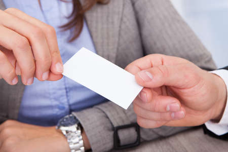 Close-up Of Businessman And Businesswoman Exchanging Visiting Card At Office Deskの写真素材