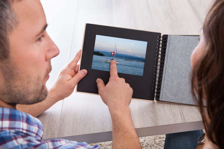 Woman Looking At Photo Album Pointed By Young Manの写真素材