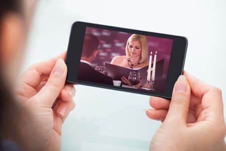 Close-up Of Person's Hand Holding Cellphone Watching Videoの写真素材