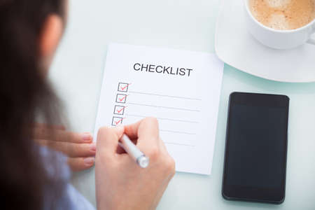 High Angle View Of A Businesswoman Marking On Checklist At Desk