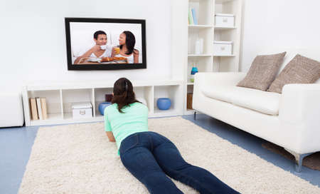 Portrait Of Young Woman Lying On Carpet Watching Television