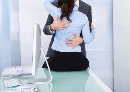 Businessman Embraces A Female Colleague Who Is Sitting Near A Desktopの写真素材
