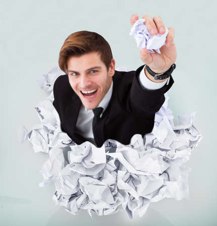 Person Under Pile Of Crumpled Paper With Hand Holding A Paperの写真素材