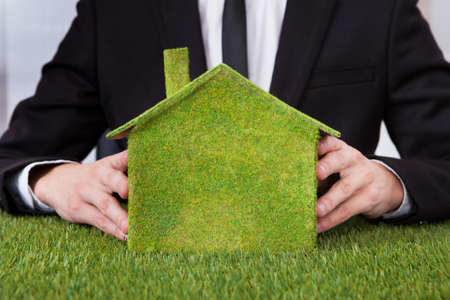 Close-up Of Businessman Holding Eco Friendly House Made From Grassの写真素材