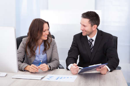 Young Businesspeople Looking At Clipboard Working At Office Desk