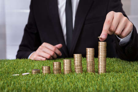 Close-up Of Businessman Stacking Coins Over Grass