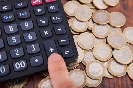 Finger Pressing Calculator Button Surrounded By Coinsの写真素材