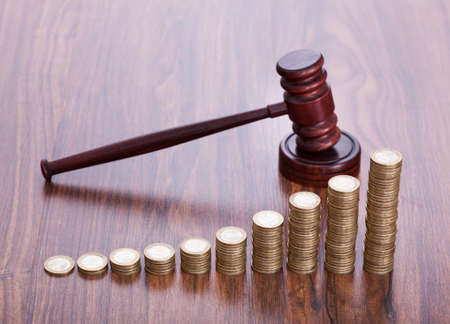 Gavel With Pile Of Coins On Wooden Deskの写真素材