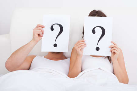 Couple Lying On Bed Holding Question Mark On Faceの写真素材