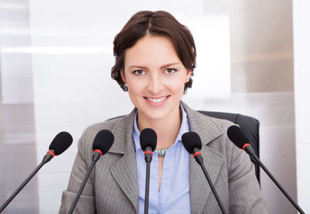 Smiling Businesswoman Holding Paper Speaking In Front Of Multiple Microphonesの写真素材
