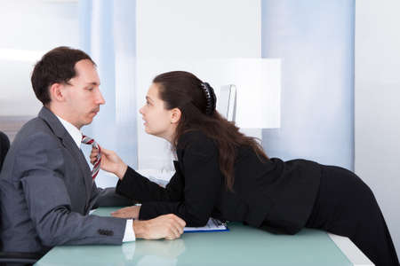 Naughty Businesswoman Holding Necktie Of Young Businessmanの写真素材