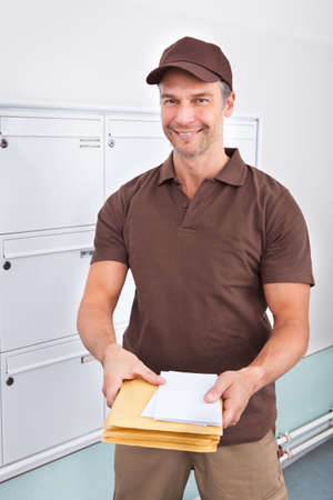 Portrait Of Happy Mature Postman Holding Lettersの写真素材