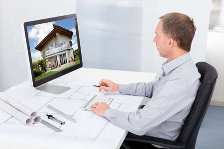 Portrait Of Mature Architect Using Computer At Office Desk
