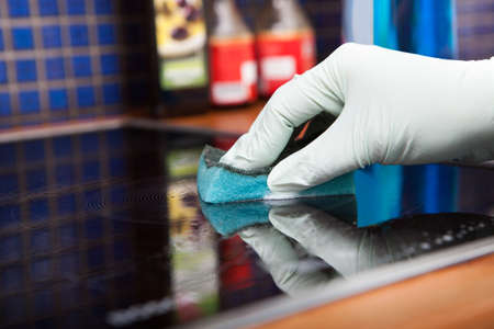 Close-up Of Person's Hand Cleaning Induction Cooker With Scrubber