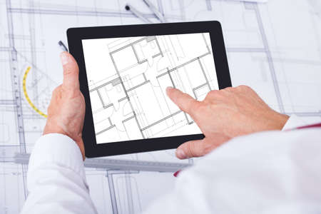 Close-up Of Male Architect Analyzing Blueprint Over Digital Tablet