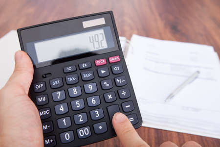 Close-up Of Person's Hand On Wooden Table Doing Calculationの写真素材
