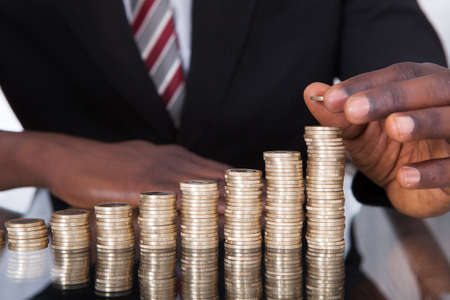 Close-up Of A Young African Businessman Stacking Coins On Deskの写真素材