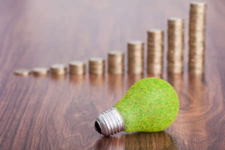 Close-up Of Ecological Bulb In Front Of Coins Stacked On Wooden Tableの写真素材