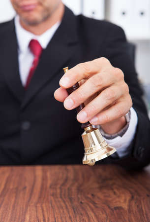 Close-up Of Businessman Hand On Wooden Table Holding Bellの写真素材