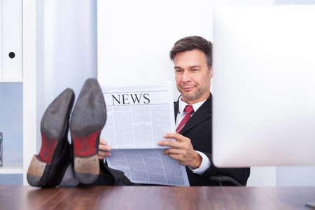 Happy Young Businessman Reading Newspaper At Office Deskの写真素材