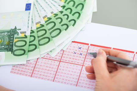 Close-up Of Hand Marking With Pen On Lottery Ticket And Banknoteの写真素材