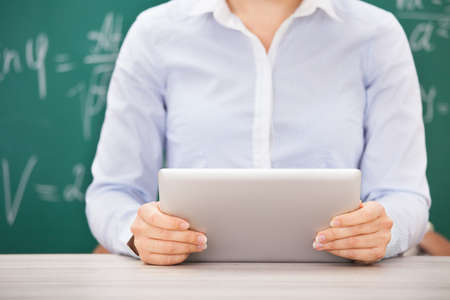 Close-up Of Female Student Using Digital Tablet In Front Of Chalkboard