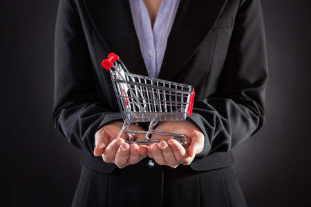 Close-up Of Businessperson Holding A Shopping Cart Over Black Backgroundの写真素材