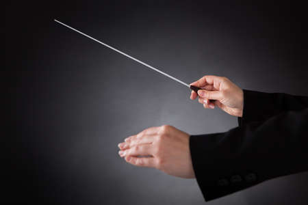 Close-up Of Female Orchestra Conductor Holding Baton Over Black Backgroundの写真素材
