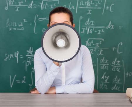 Female Student Shouting Though Megaphone Against Green Chalkboardの写真素材
