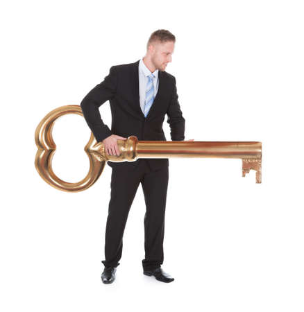 Businessman carrying an old-fashioned large brass key as he walks along conceptual of opportunity  achievement  ownership and security  isolated on whiteの写真素材