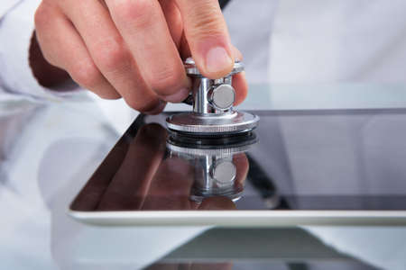 Doctor analyzing the health of tablet computer listening to the touchscreen with his stethoscope in a spoof conceptual imageの写真素材