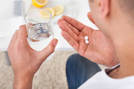 Cropped image of sick young man taking tablets with glass of water at homeの写真素材