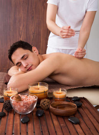 Relaxed young man with eyes closed receiving shoulder massage in spaの写真素材