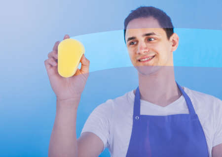 Portrait of young male servant cleaning glass with sponge over blue backgroundの写真素材