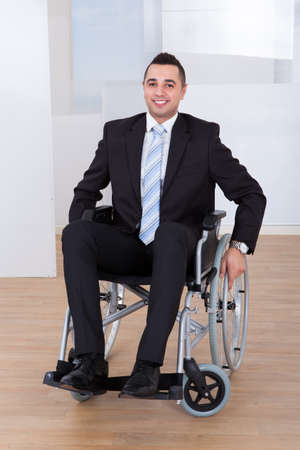 Full length portrait of happy businessman in wheelchair at officeの写真素材