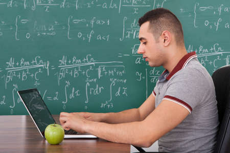 Cropped image of young male student solving math's problem on laptop by green apple on table